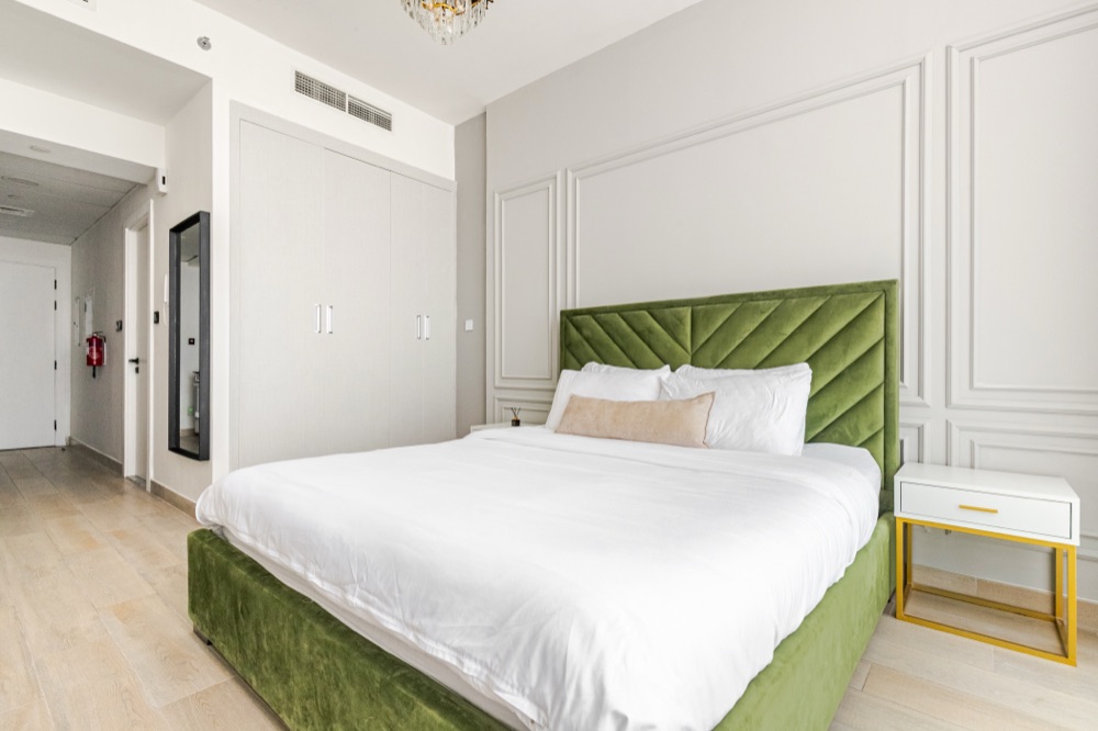 Bedroom with green velvet headboard, panelled wall and crystal chandelier